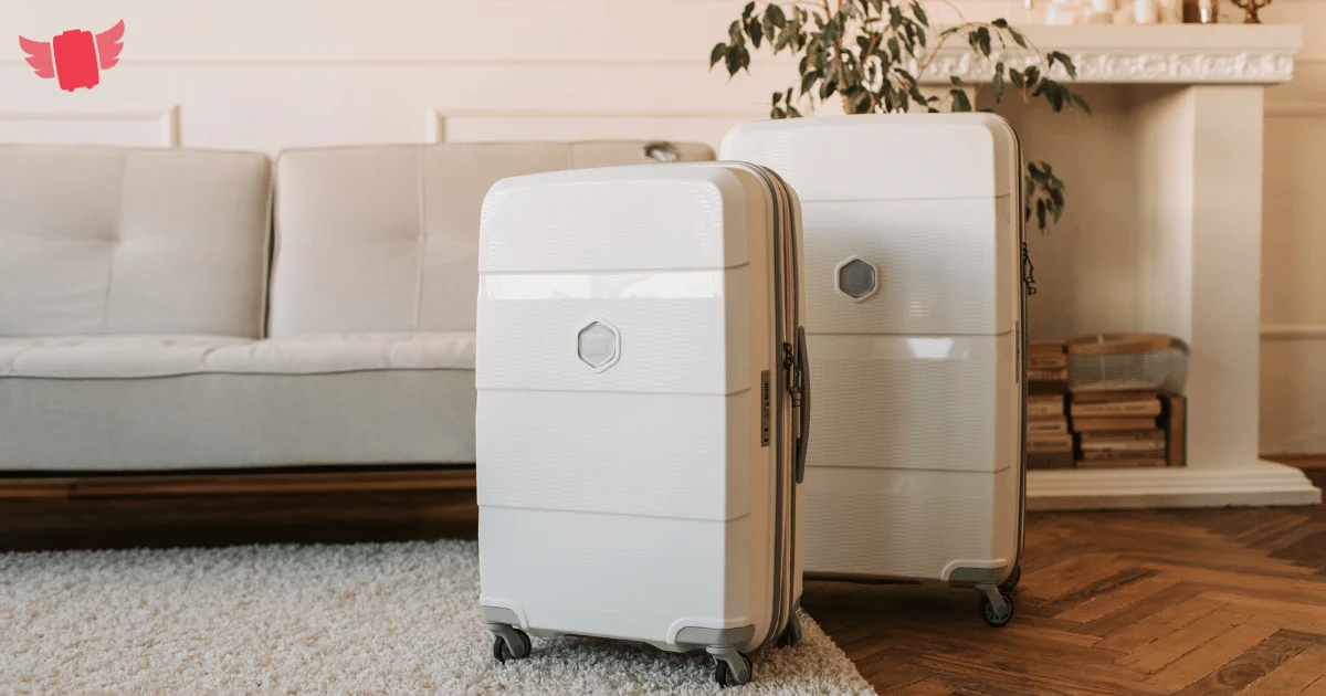 Two cream hardshell suitcases standing on a rug in a cozy living room with a sofa, plant, and fireplace